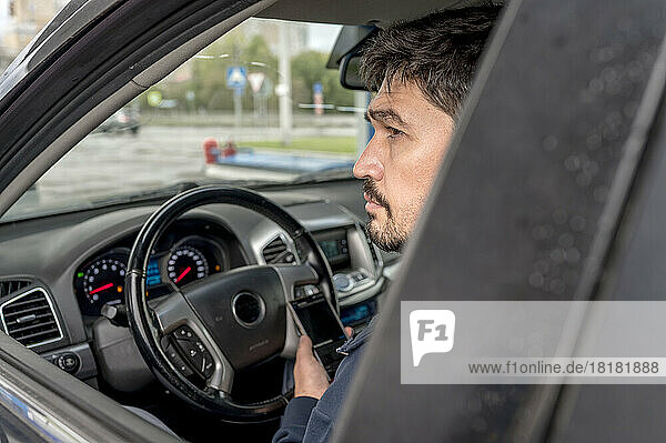 Thoughtful man with smart phone sitting in car