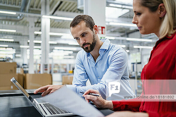 Businessman pointing at laptop with colleague at factory