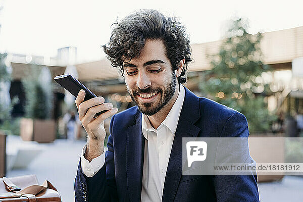 Smiling businessman wearing blazer talking on speaker phone