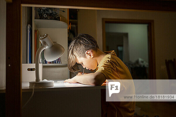 Student studying under desk lamp at home