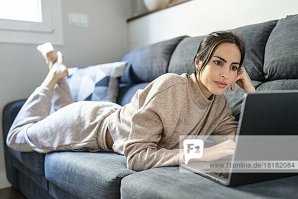 Junge Frau schaut sich zu Hause auf dem Sofa einen Film über einen Laptop an