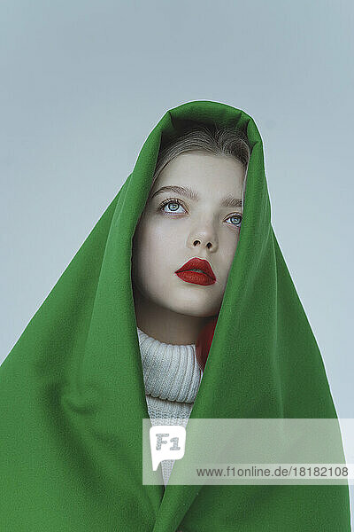 Thoughtful girl wrapped in green velvet cloth against white background