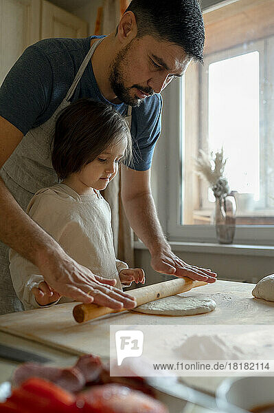 Junge mit Vater rollt Pizzateig in der Küche