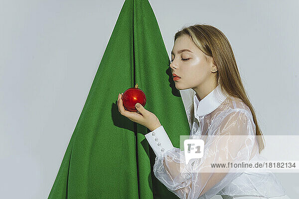Teenage girl with red ornament in front of artificial Christmas tree