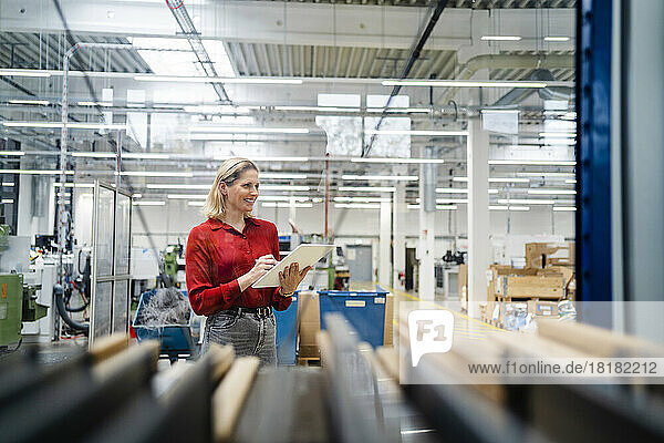 Smiling businesswoman holding tablet PC standing in factory