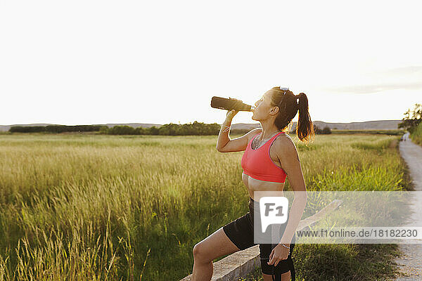 Frau trinkt an sonnigem Tag Wasser aus der Flasche