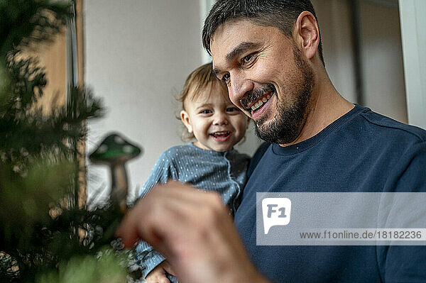 Happy father carrying son and decorating Christmas tree at home
