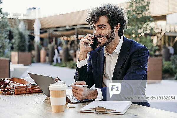 Happy businessman talking on mobile phone at table in cafe
