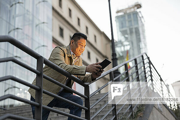 Reifer Mann benutzt Tablet-PC und lehnt am Geländer