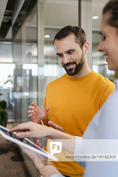 Smiling businessman gesturing by colleague using tablet PC at office