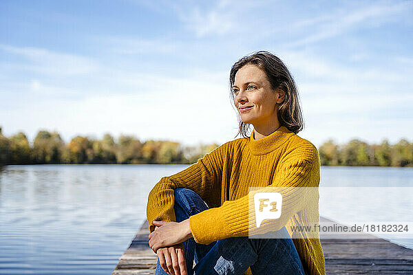 Thoughtful woman sitting on jetty under sky