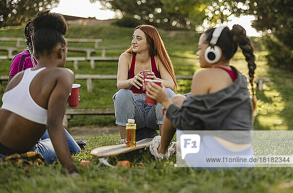 Young woman sitting with friends together having drink in park