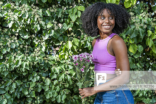 Smiling young woman holding flowers in front of plant
