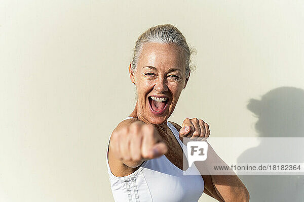 Happy woman showing fists in front of wall on sunny day