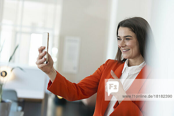 Happy businesswoman showing thumbs up on video call having through smart phone in office