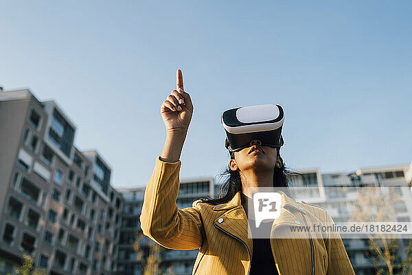 Junge Frau gestikuliert mit Virtual-Reality-Simulator unter blauem Himmel
