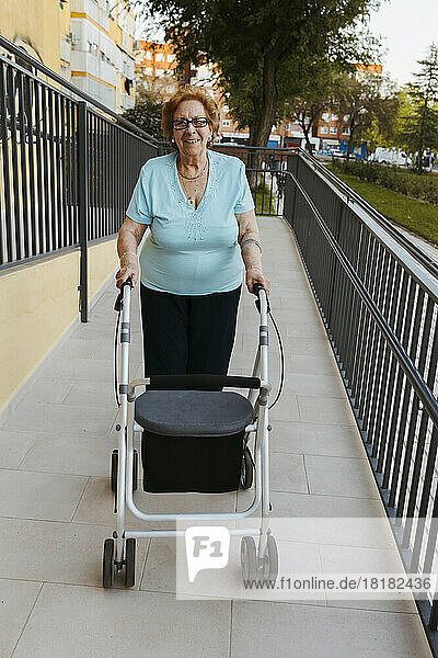 Smiling senior woman with walker on footpath