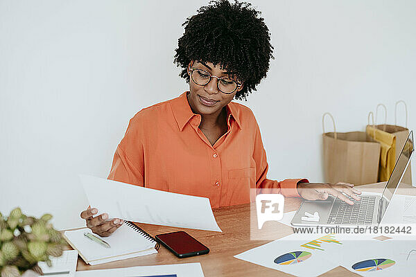Businesswoman with laptop examining documents at desk in home office