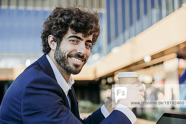 Smiling young businessman holding disposable coffee cup