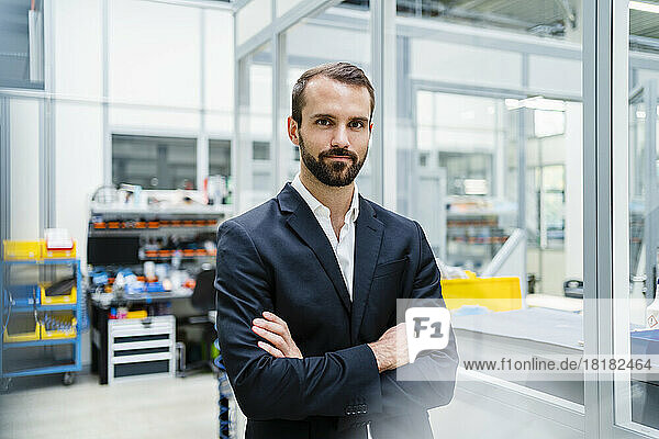 Confident young businessman with arms crossed standing in factory