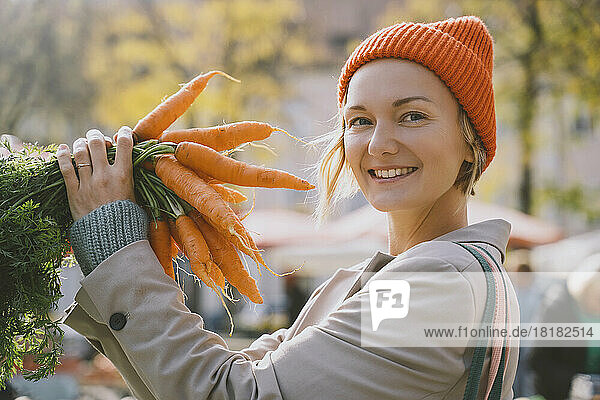 Happy woman holding bunch of carrots at market