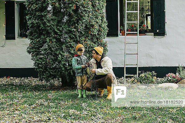 Father crouching by son in front of tree outside house