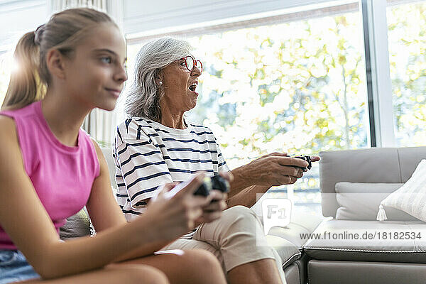 Senior woman with mouth open playing video game with granddaughter at home