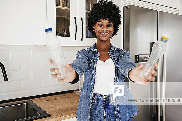 Glückliche junge Frau zeigt Plastikflaschen  die zu Hause in der Küche stehen