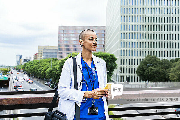 Smiling doctor with mobile phone contemplating in city