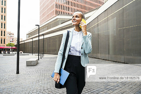 Smiling businesswoman talking on smart phone at footpath