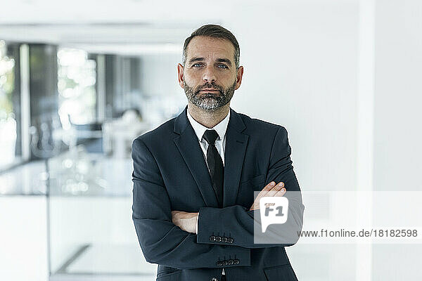Confident mature businessman with arms crossed standing in office