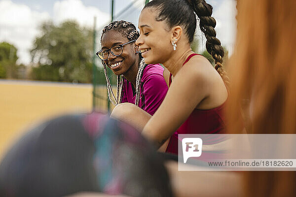 Lächelnde junge Frau sitzt mit Freunden im Sportplatz