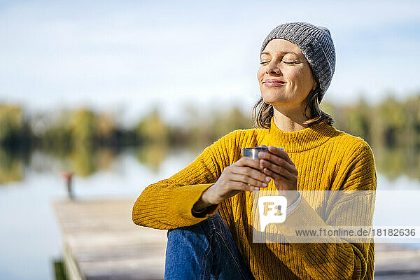 Smiling woman sitting with coffee cup on sunny day