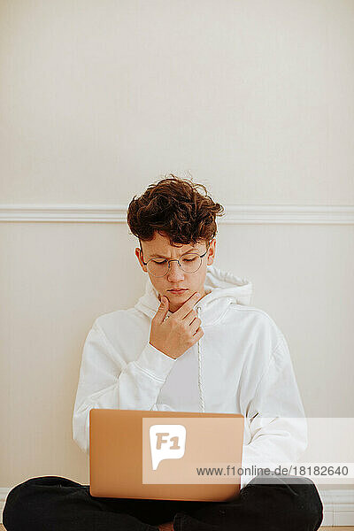 Junge sitzt zu Hause mit Laptop vor der Wand