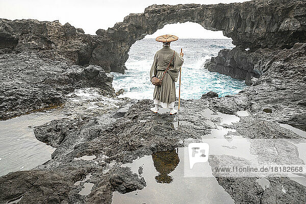 Monk with stick standing in front of rock arch