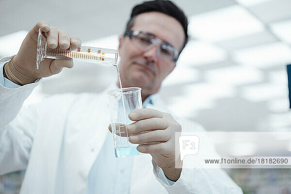 Chemist pouring solution from test tube to flask in laboratory