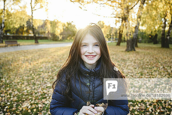 Lächelndes Mädchen in warmer Kleidung steht im Herbstpark