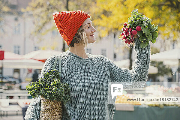 Smiling woman wearing sweater looking at radish at market