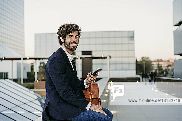 Contemplative businessman with smart phone sitting on wall