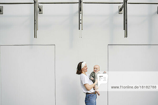 Mother carrying smiling boy in front of wall