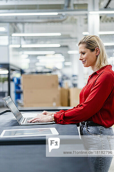 Smiling businesswoman using laptop standing at factory