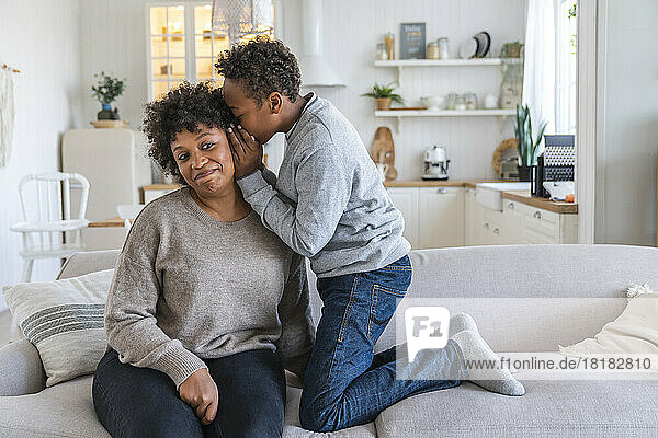 Son whispering into mother's ear at home