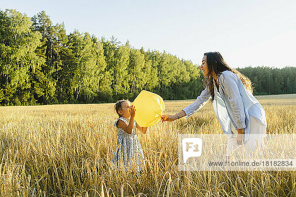 Playful woman with daughter holding garbage bag balloon standing at field
