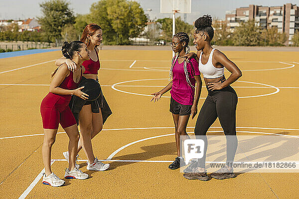 Young friends talking at basketball court on sunny day