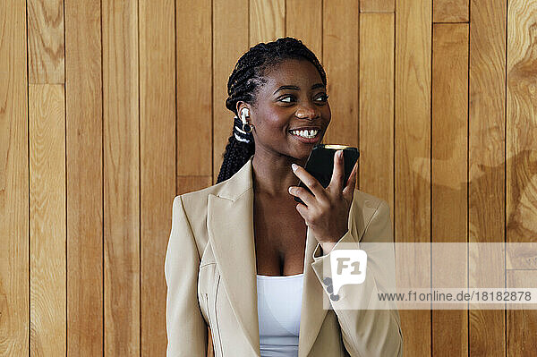 Happy businesswoman talking on smart phone in front of wooden wall