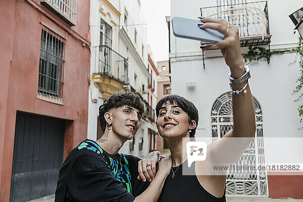 Smiling woman with boyfriend taking selfie through mobile phone in front of buildings