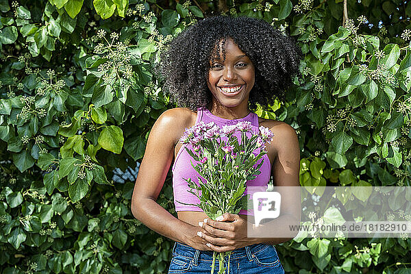 Happy young woman holding flowers in front of plant