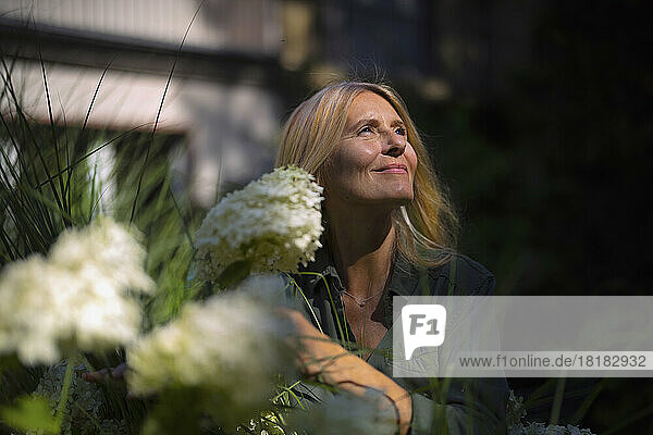 Smiling mature woman standing by flowering plant in garden
