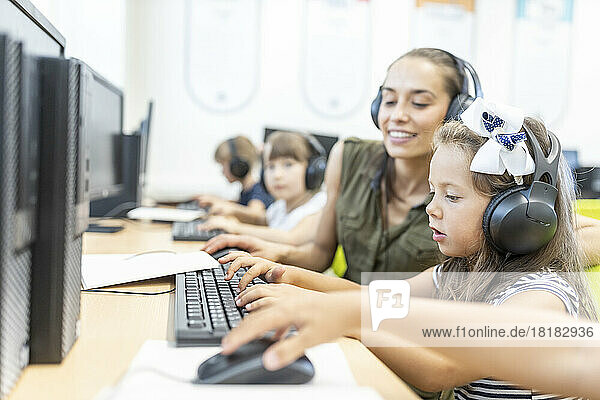 Girl wearing headphones using computer with teacher in class at school