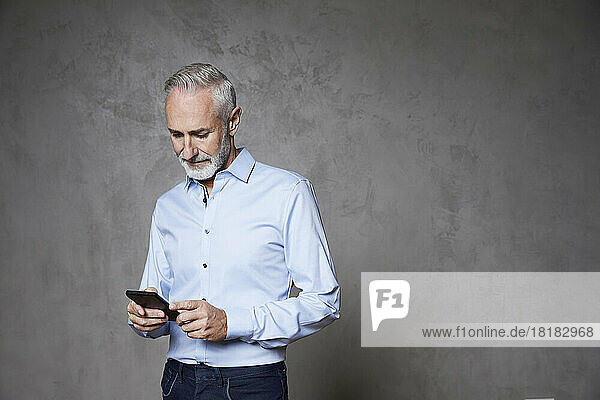 Mature man using smart phone standing in front of grey background